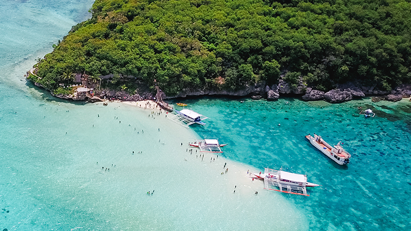 Aerial view of sandy beach with tourists swimming in beautiful clear sea water of the Sumilon island beach landing near Oslob, Cebu, Philippines